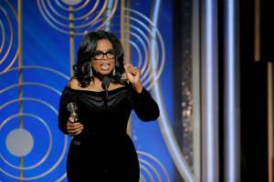 Oprah Winfrey speaking into a microphone will holding her Golden Globe award in her right hand. 